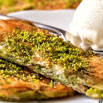 A golden-brown Turkish Katmer pastry sliced and topped with ground pistachios