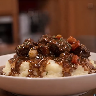 A white bowl filled with classic French Beef Bourguignon featuring tender beef chunks, mushrooms, and pearl onions in a rich red wine sauce, served next to a crusty baguette